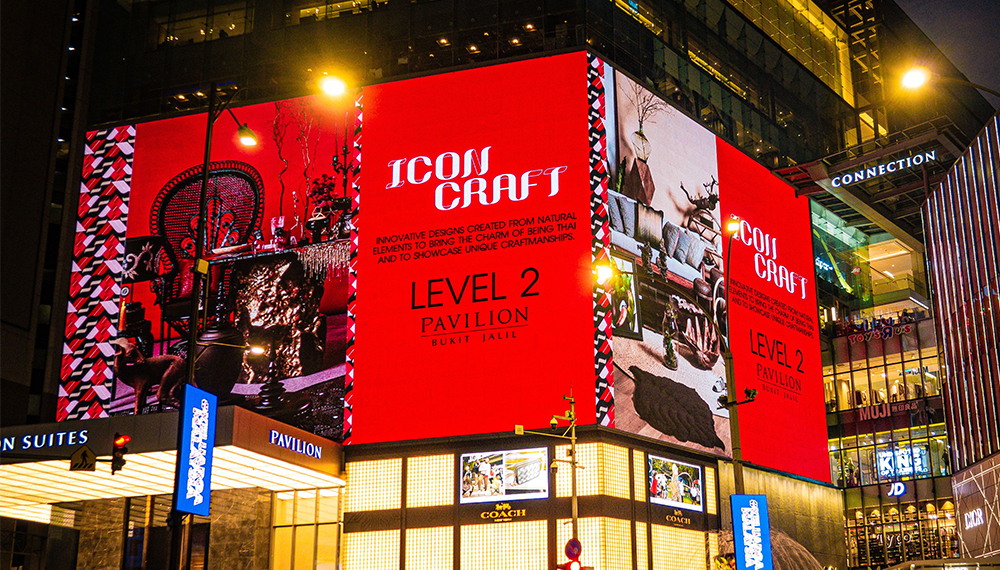 Nighttime urban scene with a large red billboard reading Icon Craft Level 2 Pavilion dominating a building façade in a shopping district.