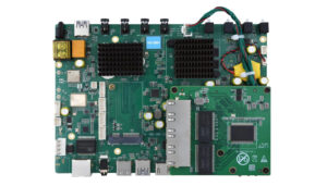 Green computer motherboard PCB with two black cooling heat sinks, RAM/CPU area, various capacitors, connectors, and USB ports along the bottom edge.